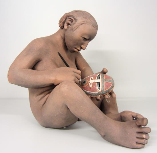 A clay sculpture of a person sitting and painting a mask.