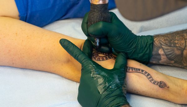 Closeup of Lambert tattooing a snake on his client's forearm