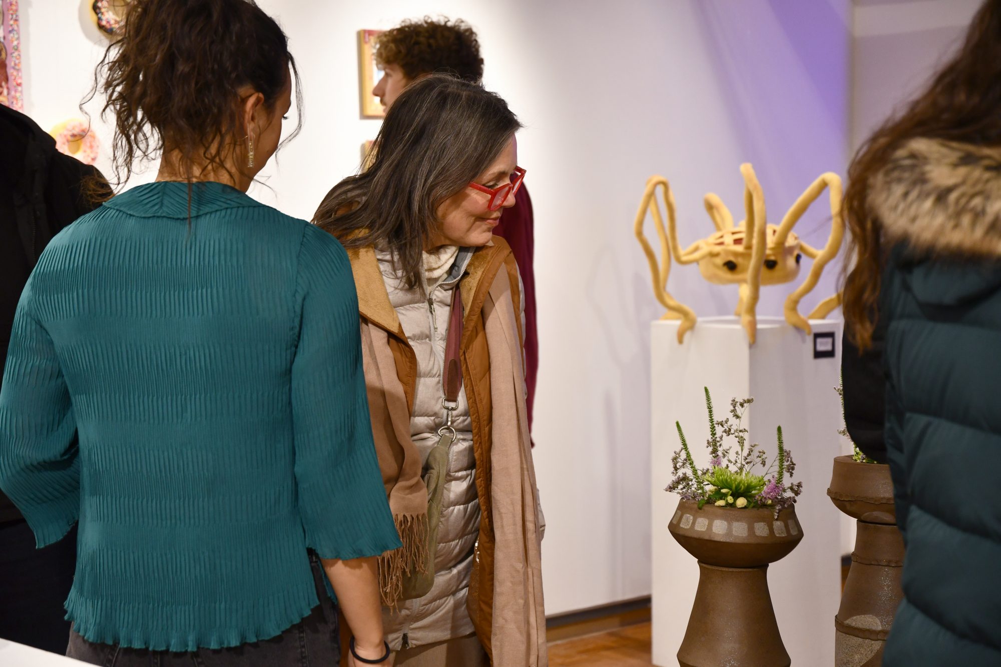 Visitors admiring artwork in a gallery with a plant sculpture.