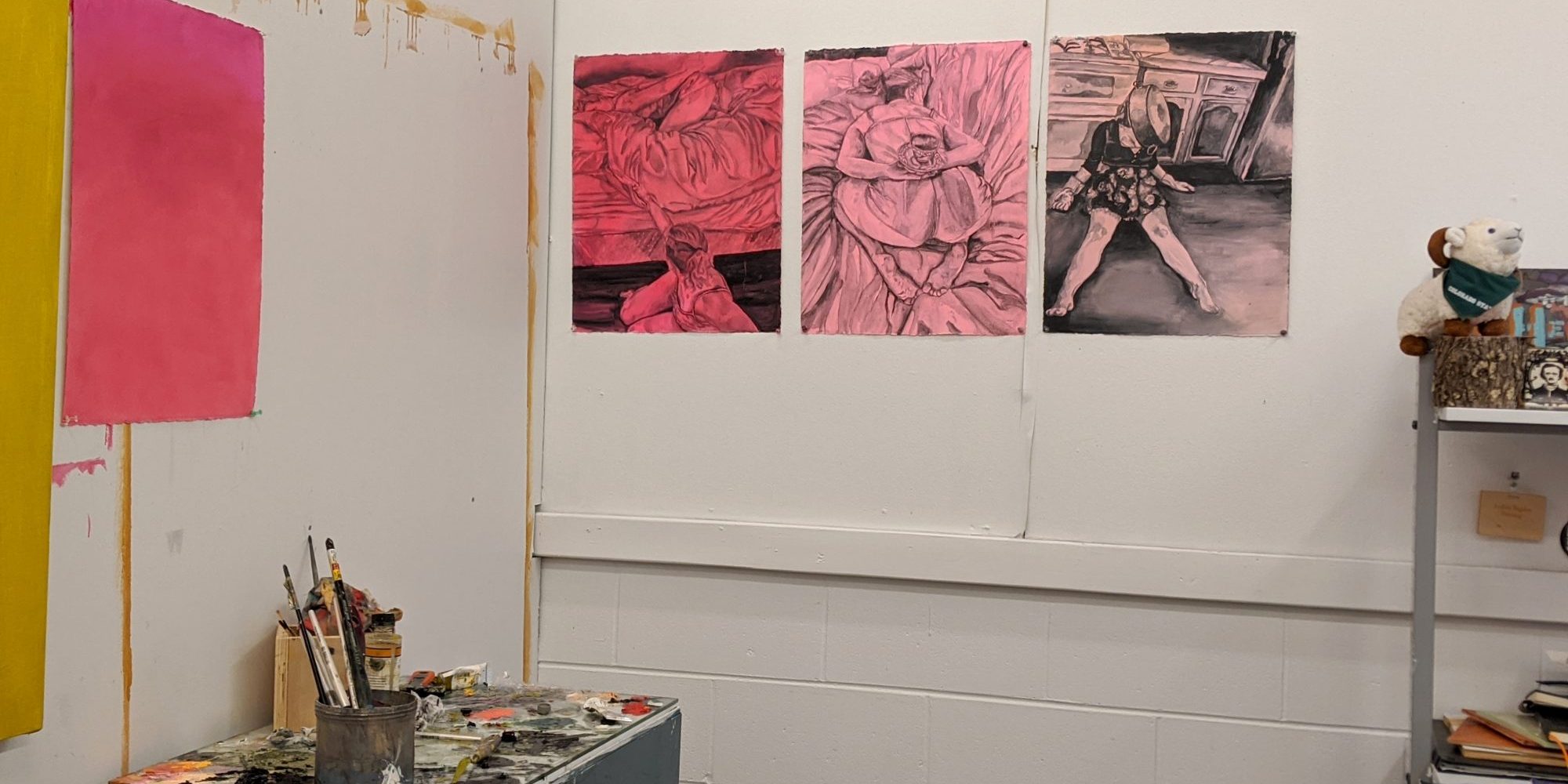 Andrea Bagdon's Painting studio with pink and yellow images on white cinder block walls.