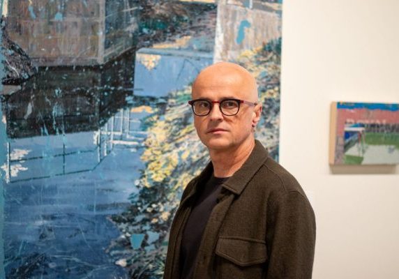 Professor Marius Lehene standing in front of his artwork at a gallery exhibition.
