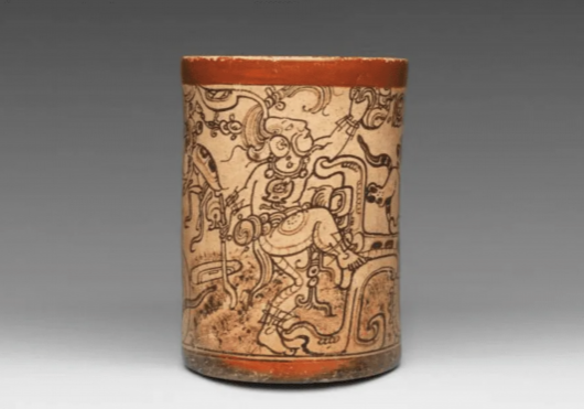 Ancient Maya cylindrical pottery vessel decorated with intricate painted figures and patterns in brown and red tones.